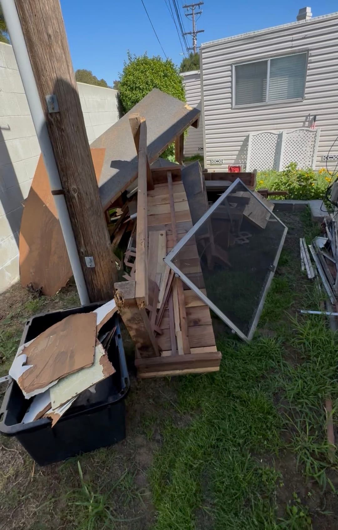 Discarded wood and debris in a messy backyard, including broken furniture and trash bin.