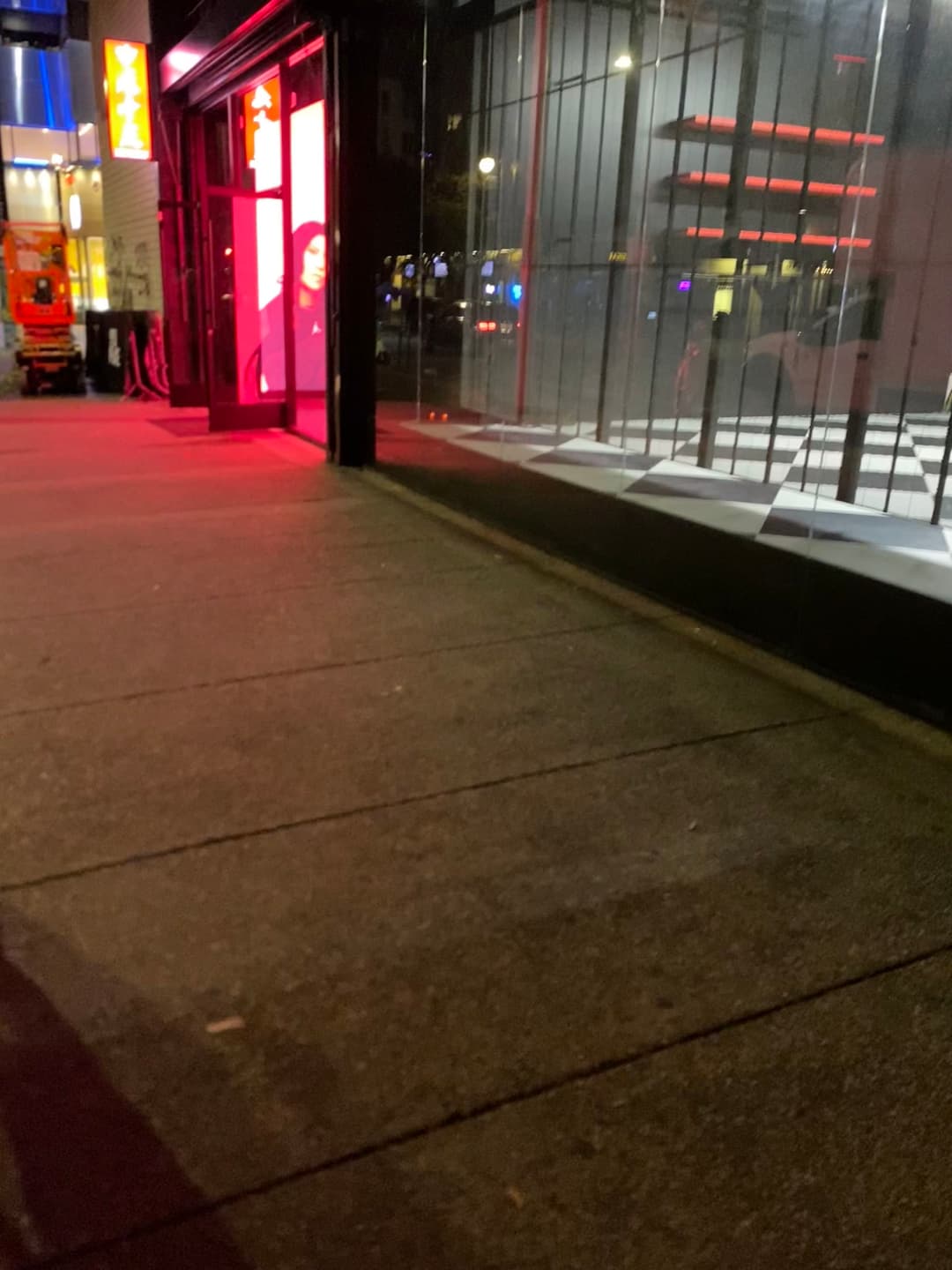 Vibrant city street at night with a red-lit storefront and reflections in the glass.