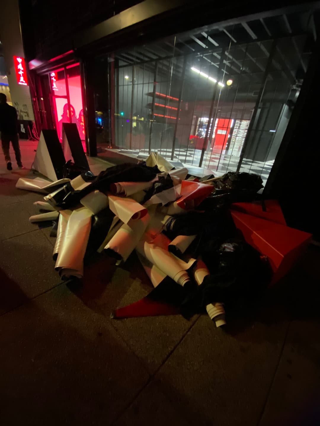 Discarded signage and debris piled outside a storefront at night, with red lighting visible inside.