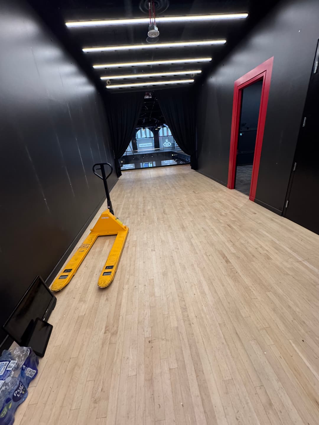 Empty hallway with wooden flooring, black walls, red door, and pallet jack ready for use.