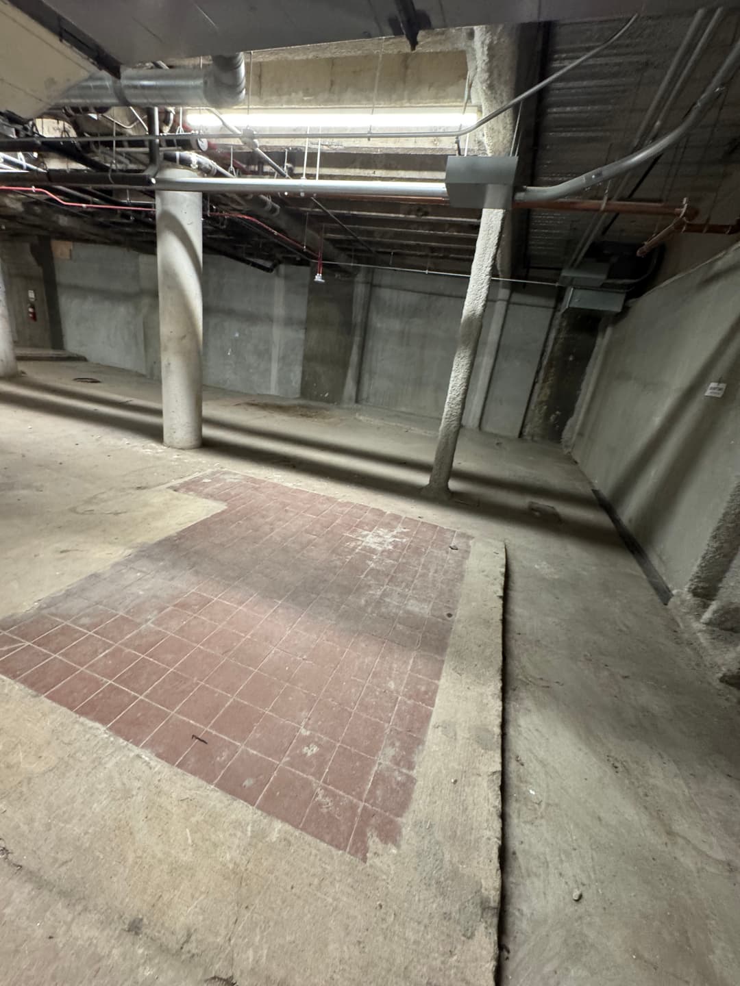 Abandoned basement with concrete walls, pillars, and a section of tiled flooring.