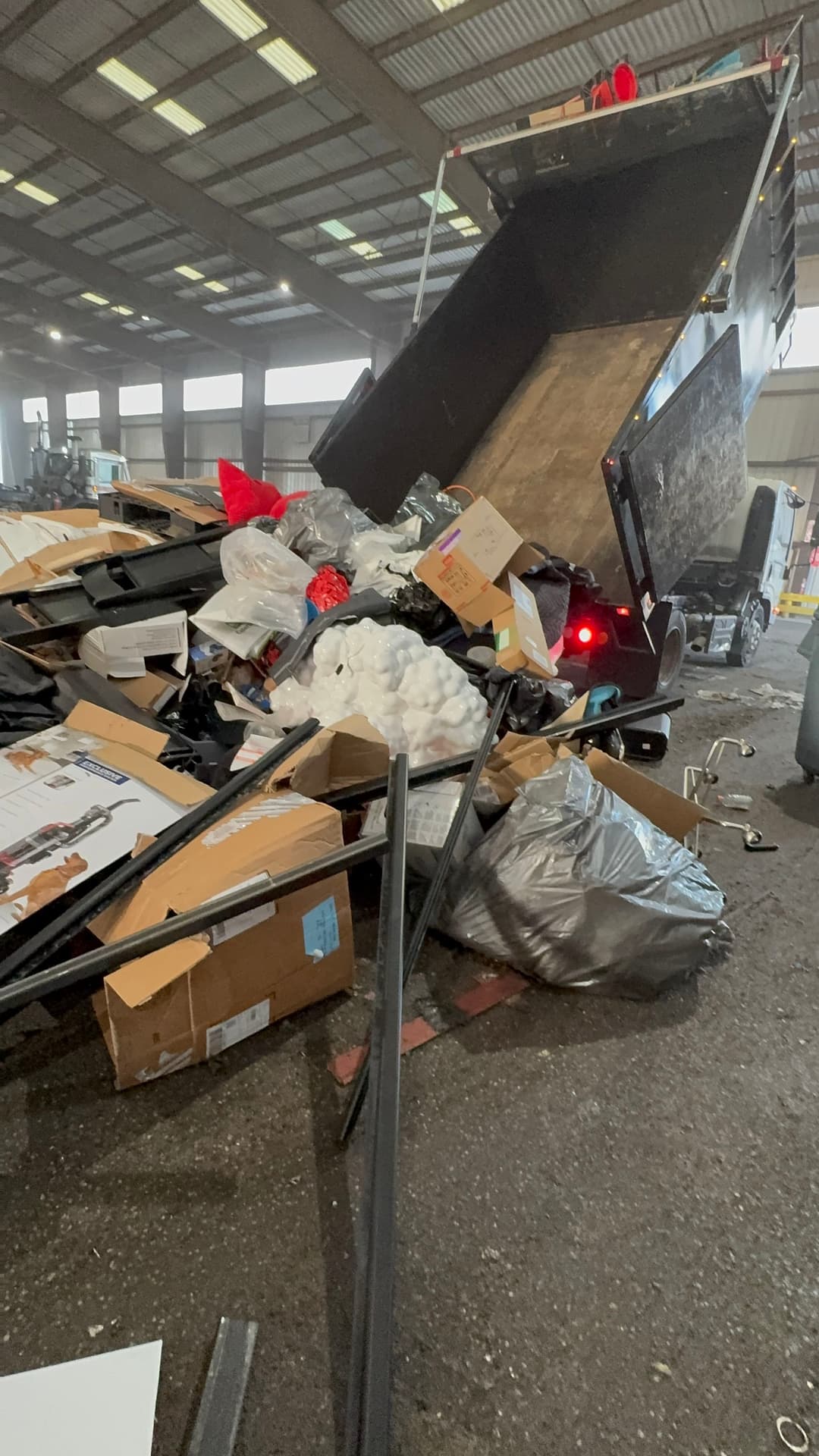Dump truck unloading mixed commercial waste including cardboard and plastic bags in a warehouse.