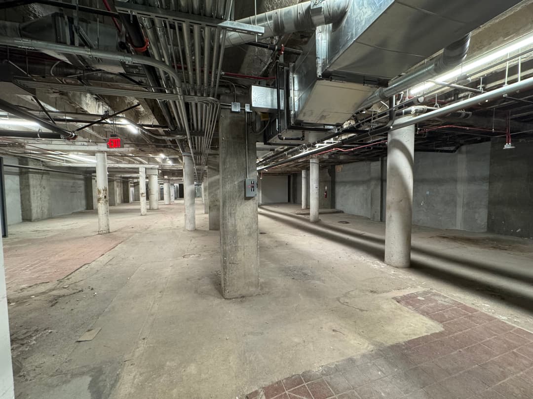 Spacious, empty basement with exposed pipes and concrete pillars and floors.