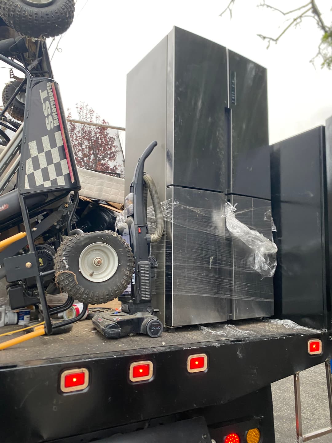 Black refrigerator and vacuum on a truck, with off-road vehicle parts in the background.