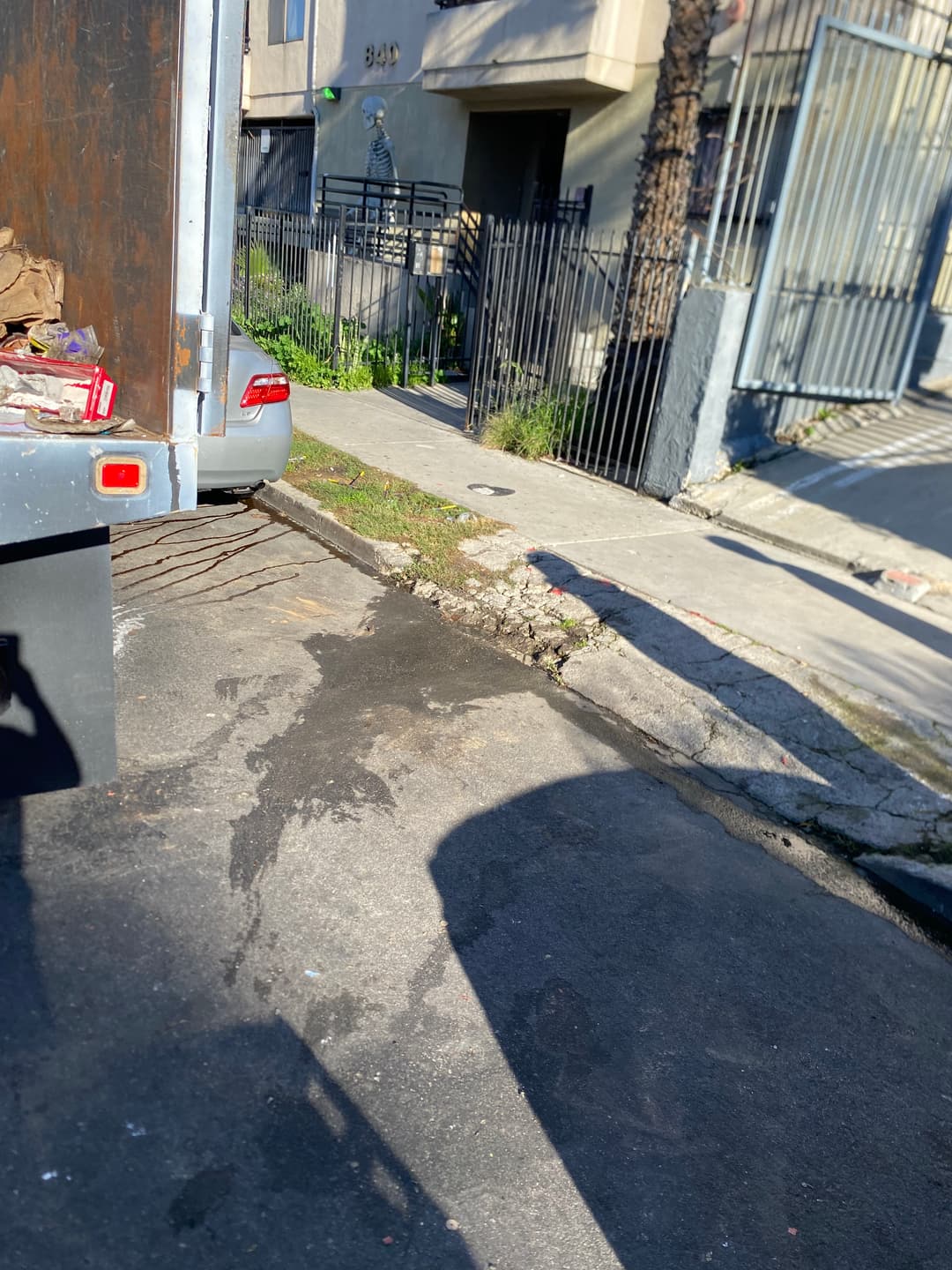 View of a truck rear with spilled garbage on a city street near a fenced property.