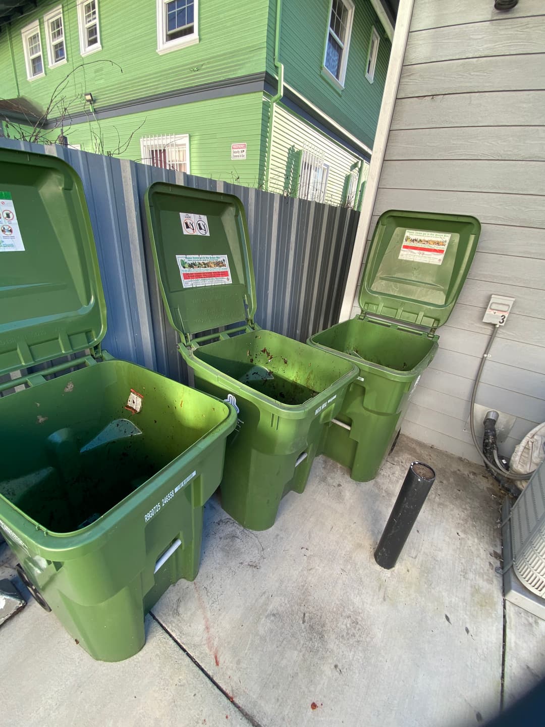 Green compost bins lined up next to a house, showing signs of organic waste disposal.