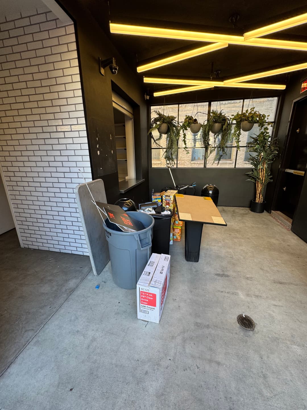 Indoor hallway with trash bins, a table, and plants under modern lighting.