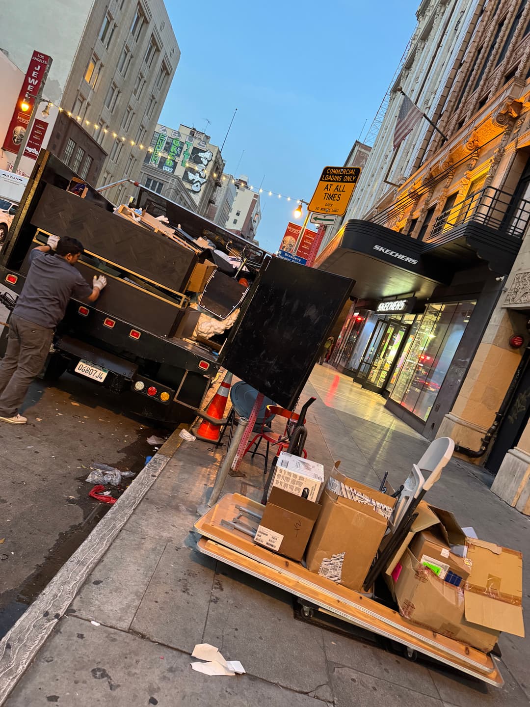 Waste disposal truck on a city street, with cardboard boxes and trash piled nearby.