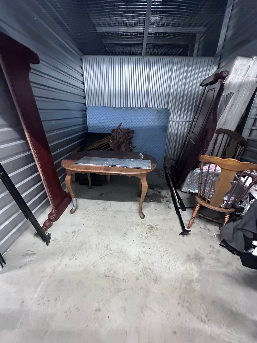Storage unit clutter with a vintage wooden table, chairs, and various old furniture pieces.