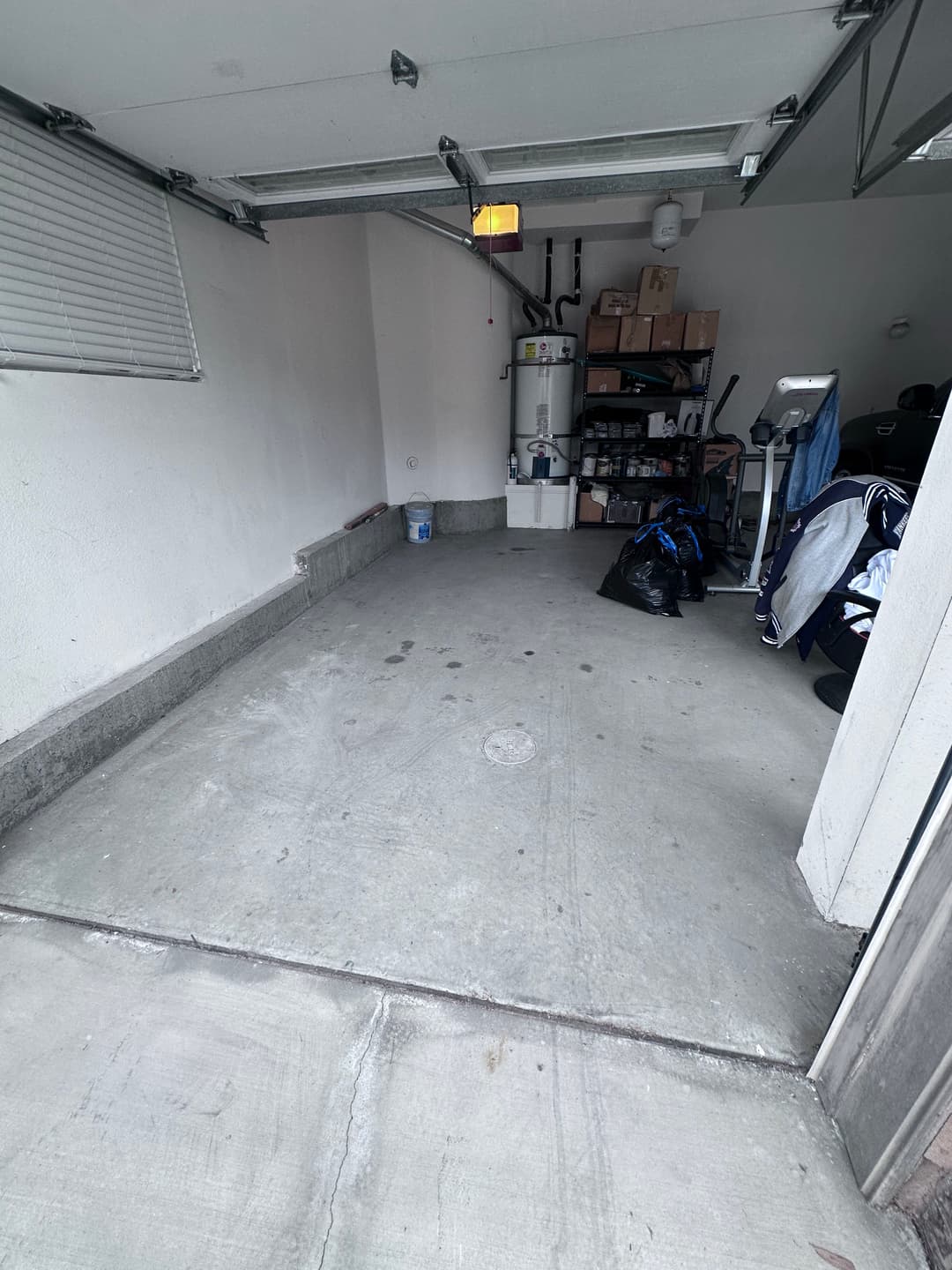 Empty garage space with concrete floor, storage shelves, and few items against the wall.