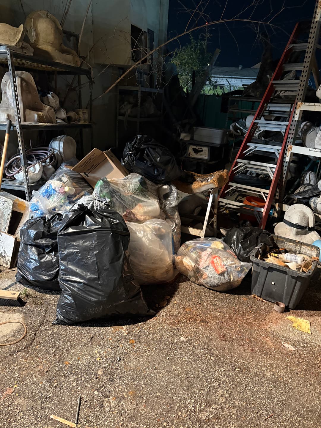Cluttered storage area filled with black garbage bags and debris at night.