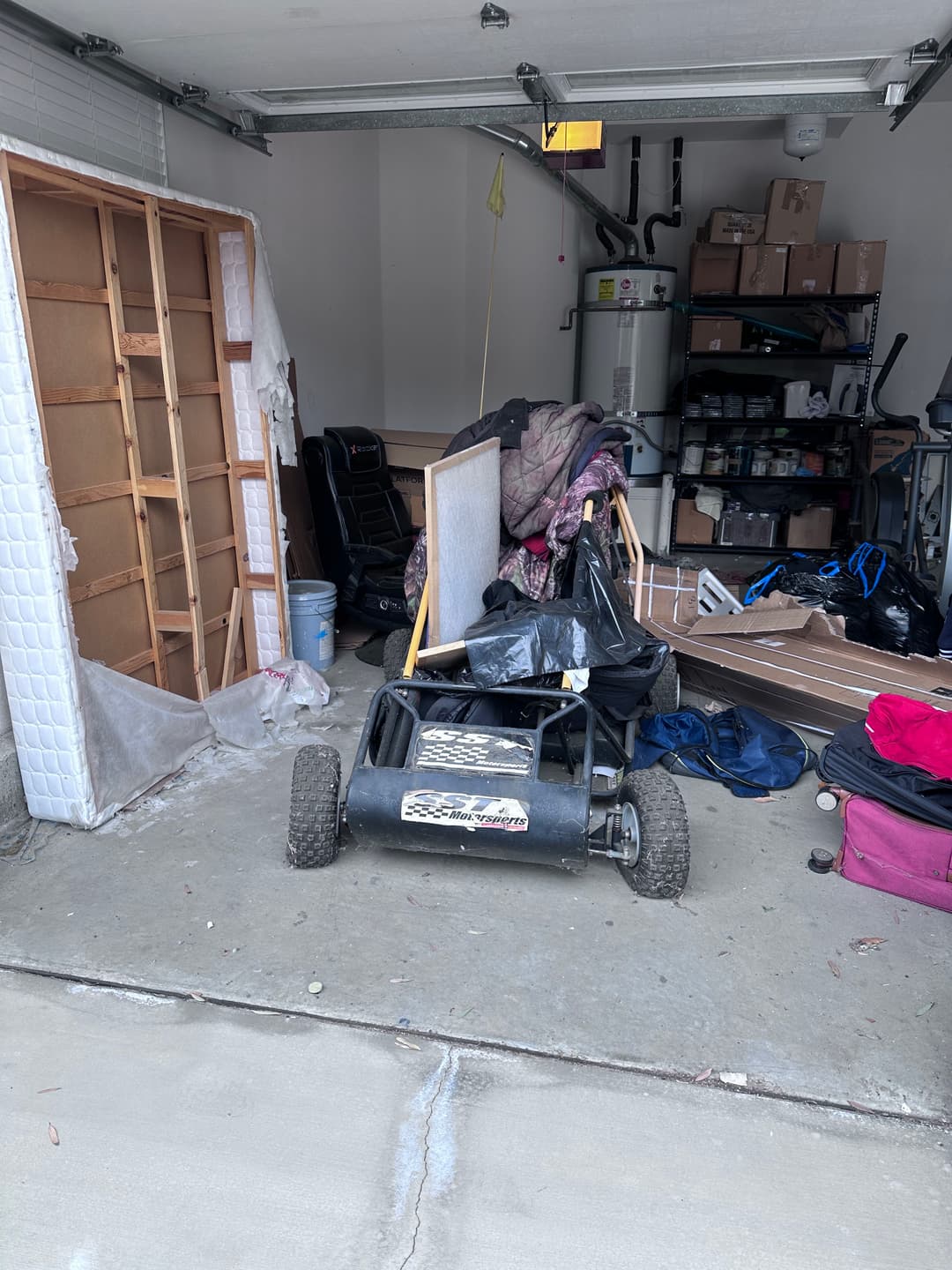 Cluttered garage with a golf cart, tools, and disorganized boxes and furniture.