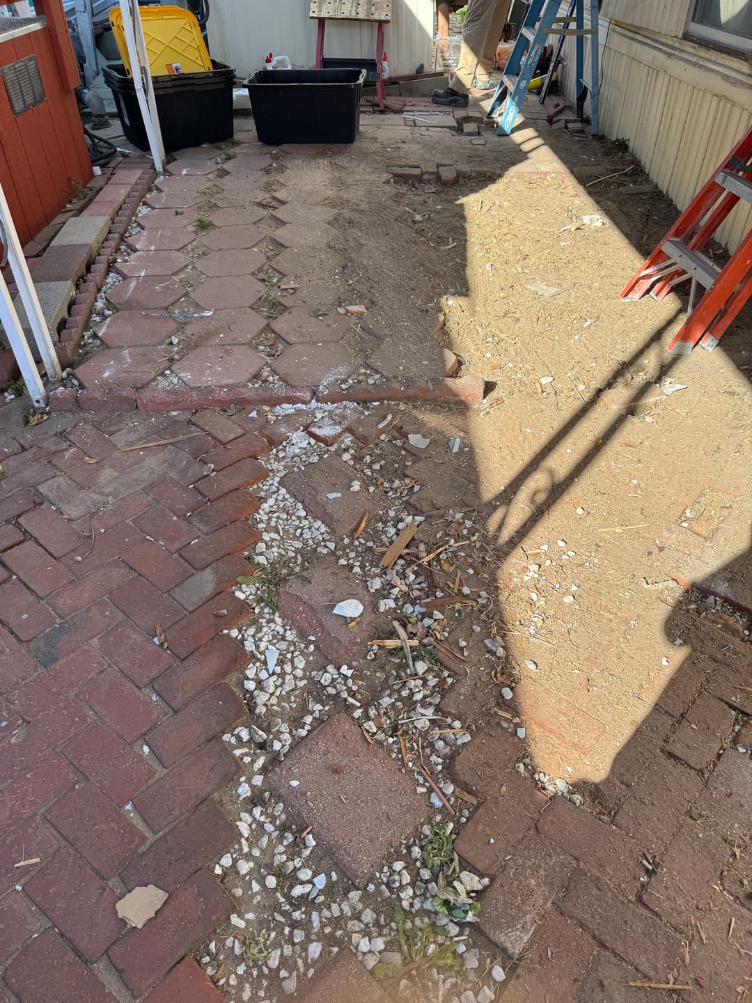 Pathway with uneven bricks and exposed soil, tools and ladders in background, construction site.