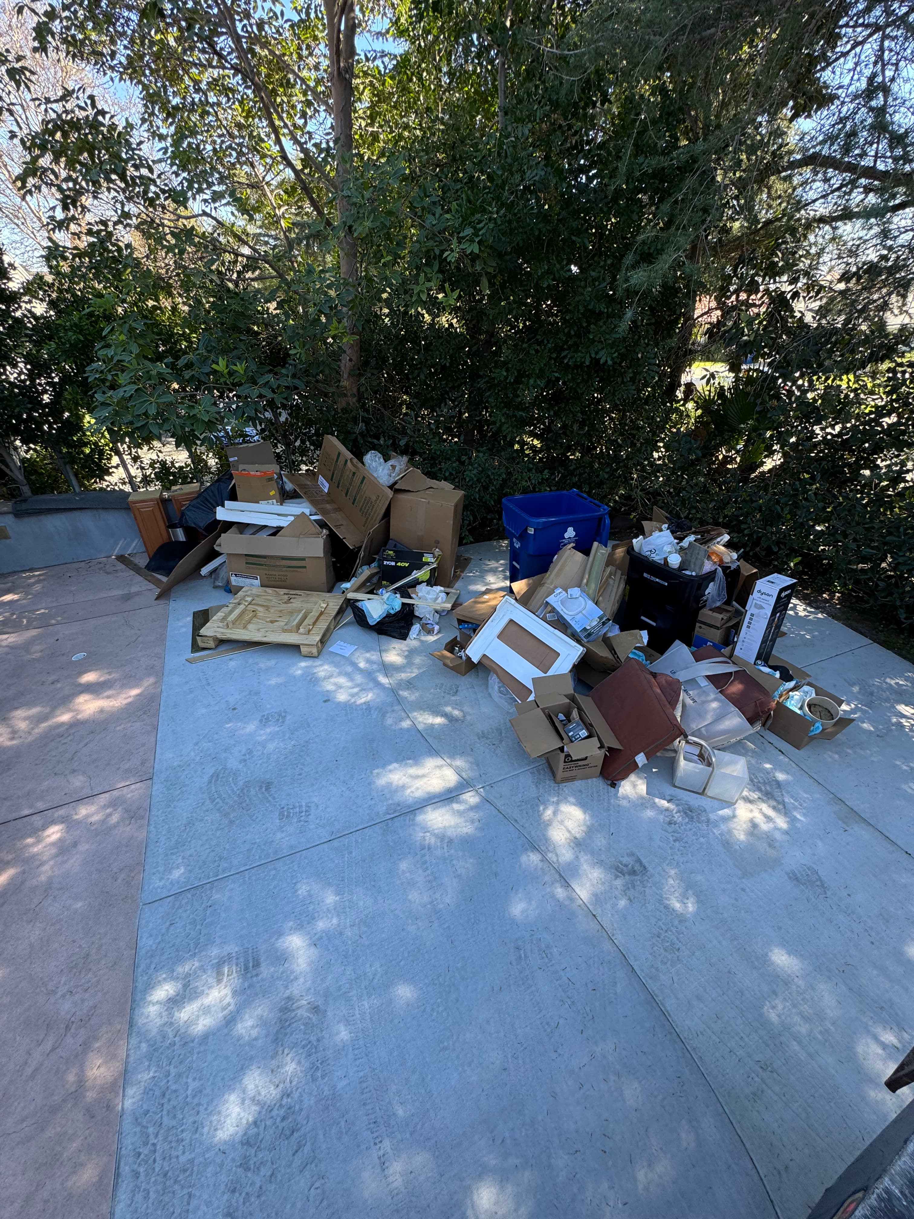 Discarded cardboard boxes and trash piled on a patio surrounded by greenery.