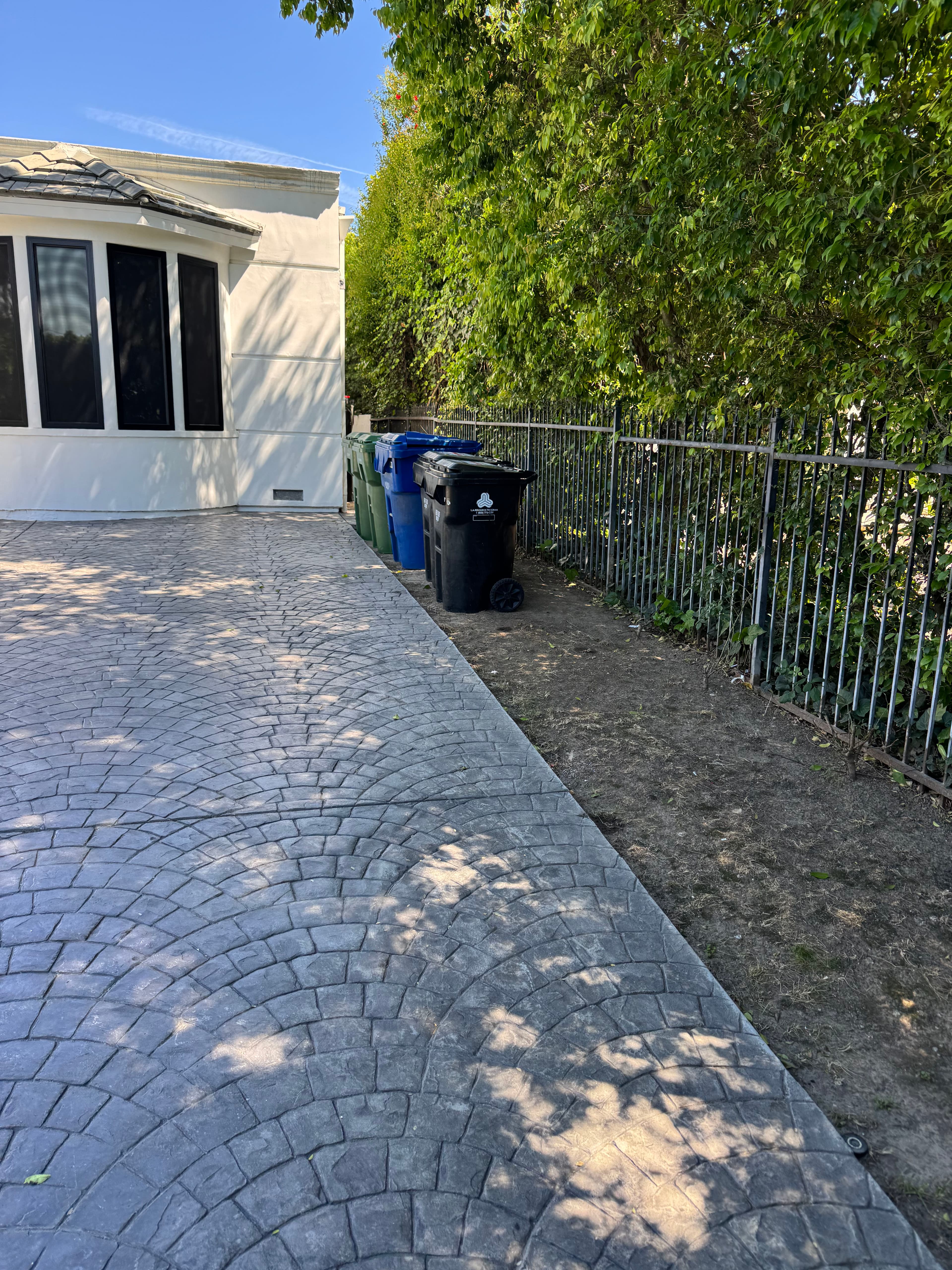 Residential driveway with concrete pavers, green and blue trash cans beside a fence.