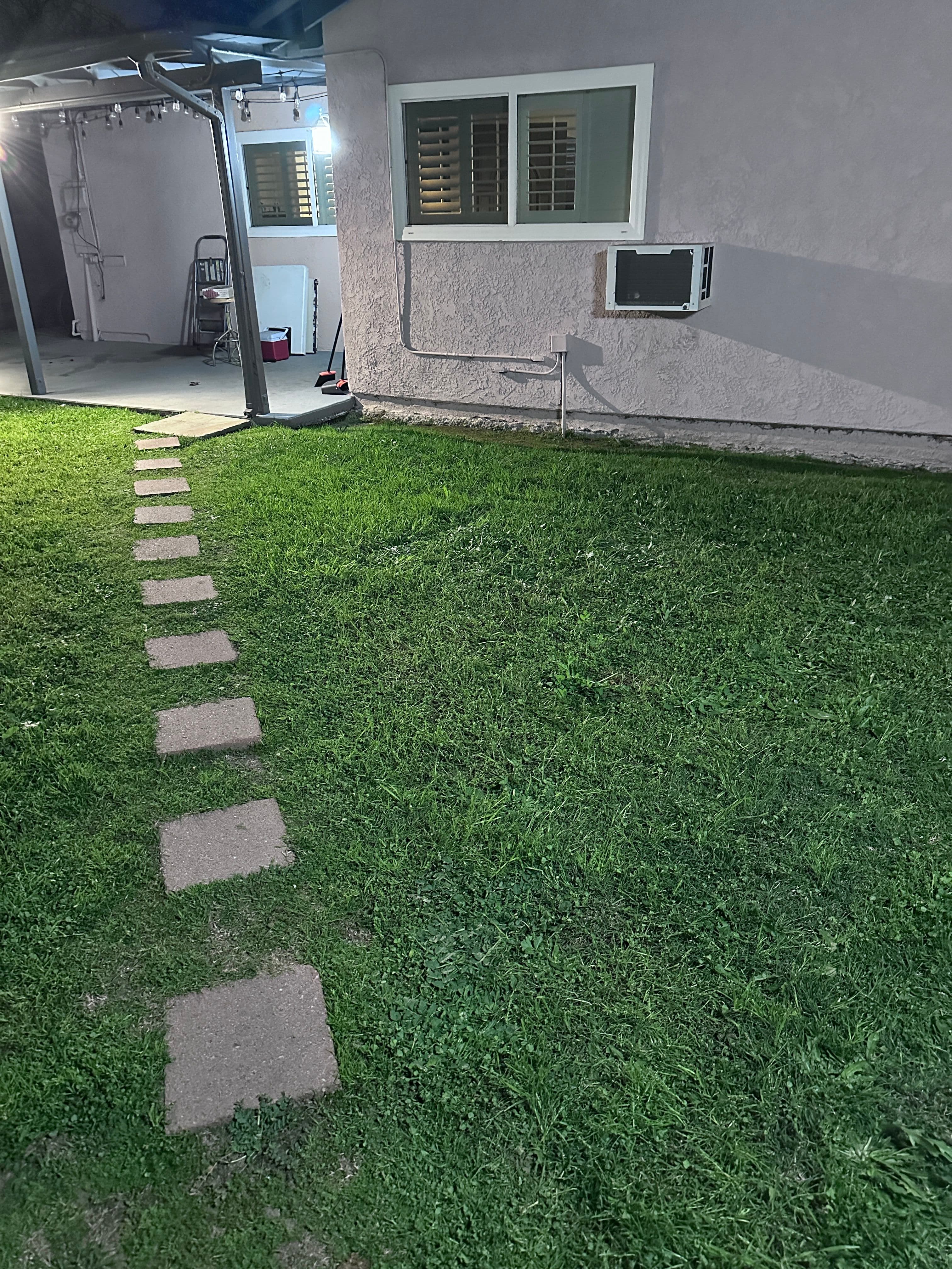 Pathway of stepping stones leading to an air conditioning unit beside a pink house at night.