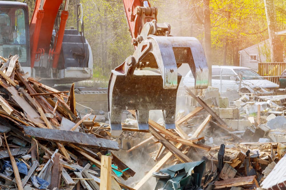 Excavator clawing debris at a construction site with sunlit background and scattered materials.
